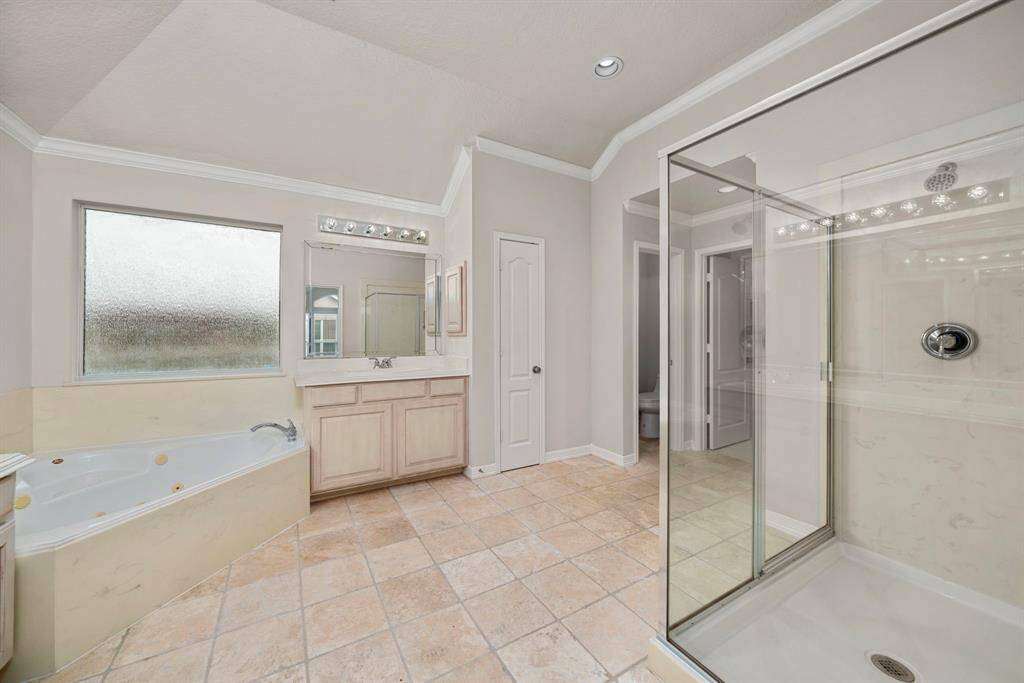 This bathroom view highlights the glass-enclosed walk-in shower and private water closet. Natural light streams in through the frosted window, creating a bright and spa-like retreat.