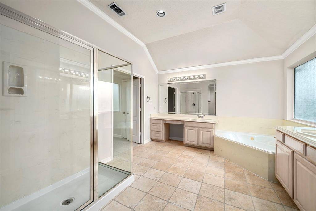 This angle shows the spacious glass-enclosed shower, wraparound vanities, and soaking tub all illuminated by natural light from a frosted privacy window. Thoughtful design offers both luxury and convenience.