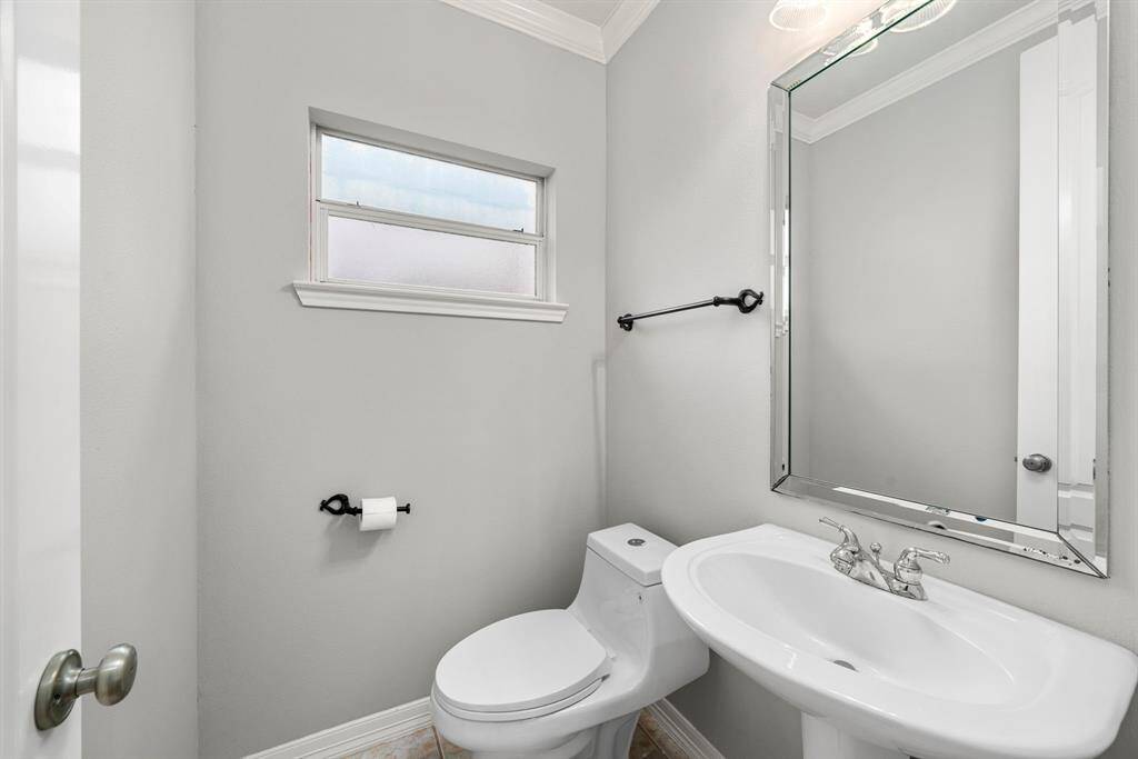 The conveniently located powder bath on the main level features a pedestal sink, sleek fixtures, and a framed mirror. A frosted window adds privacy while maintaining soft natural light.
