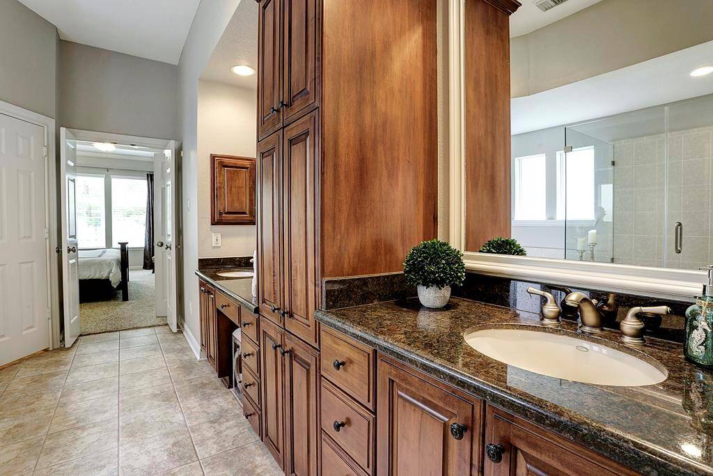 A pair of French doors reveals an en-suite primary bath with a generous amount of cabinetry, dual sinks, vanity and granite countertops.