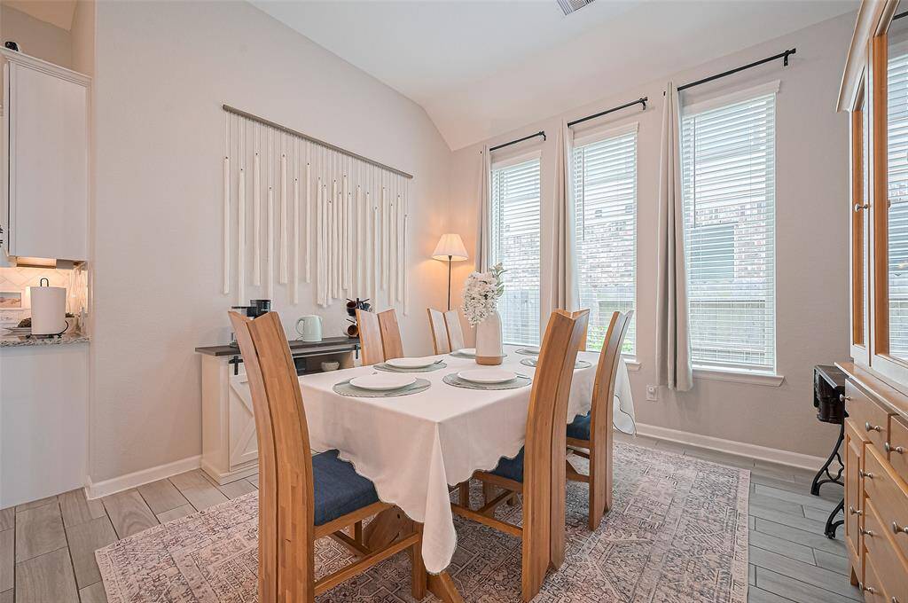 Dining area is filled with natural light from a trio of tall windows, creating a bright and welcoming setting for meals. Neutral tones and clean lines provide a calm, versatile backdrop that complements any style.