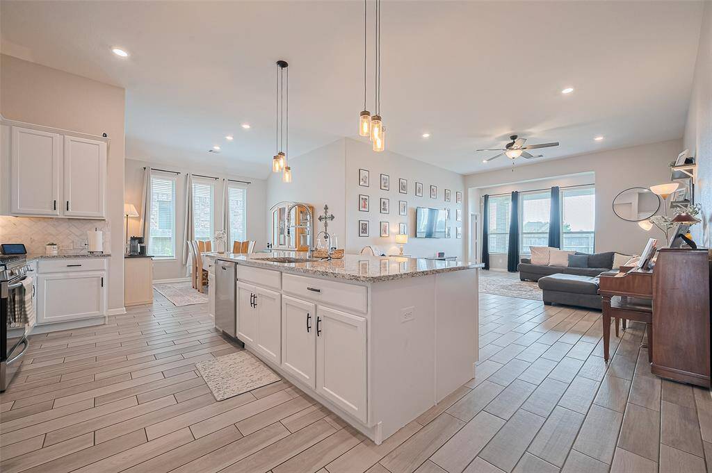 Beautiful view of the open-concept kitchen and living area featuring a spacious island with storage, pendant lighting, and seamless tile flooring throughout. Natural light pours in from the surrounding windows, creating a bright and inviting atmosphere.