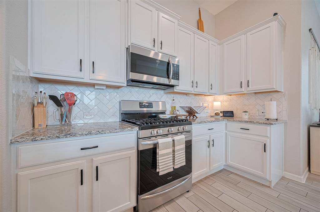 A closer angle of the oven and stove shows the symmetry of the appliances with the cabinetry. A decorative tile backsplash and under-cabinet lighting add both charm and functionality.