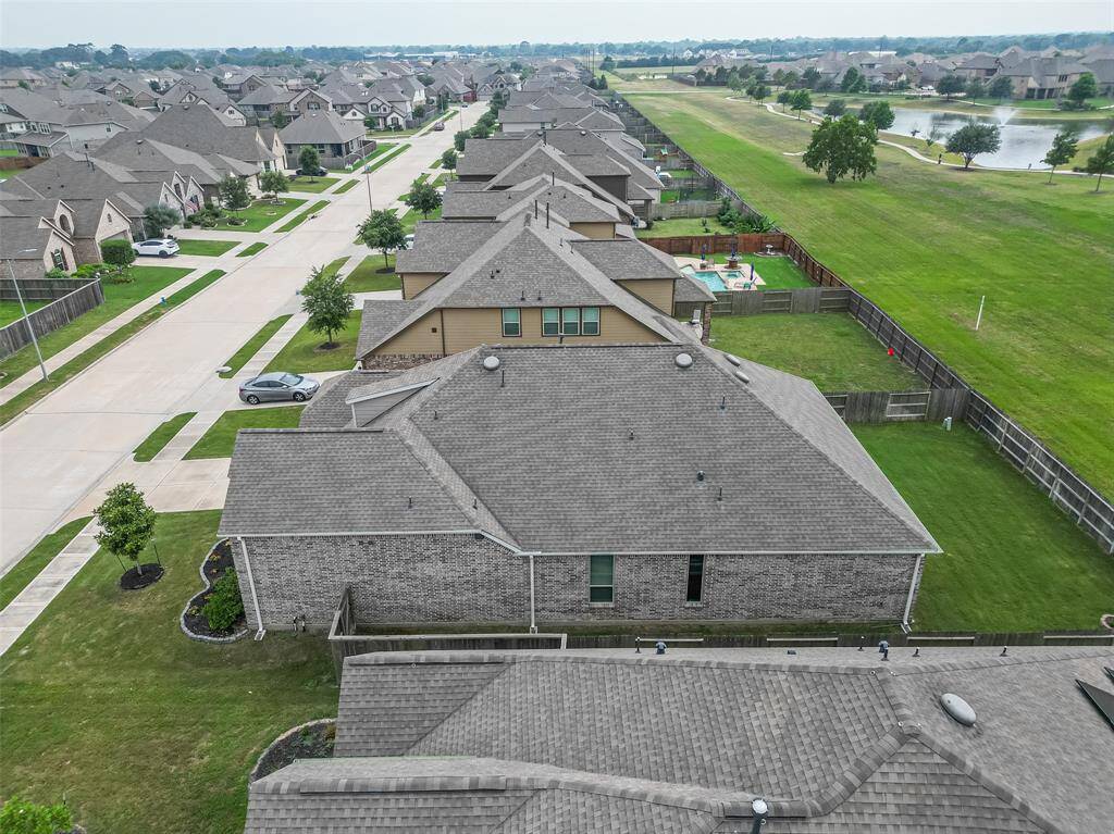 Aerial view showcases a meticulously kept neighborhood with spacious lots, tree-lined sidewalks, and uniform brick homes. The featured property enjoys added privacy with no back neighbors and direct access to a serene greenbelt and walking trail. Its all-brick exterior and well-manicured lawn enhance both its durability and curb appeal.