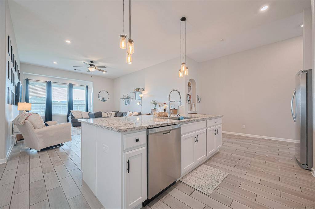This view highlights the spacious flow from the kitchen into the living area, great for everyday living. Pendant lighting and stainless appliances accent the generous island and open-concept layout.