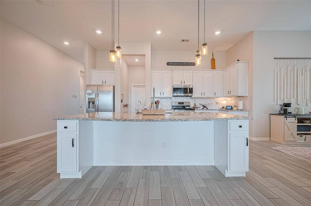 This image captures the full width of the expansive kitchen island, providing ample prep space and casual seating. The overhead lights add a warm touch, while the backdrop highlights the kitchen’s modern layout and functionality.