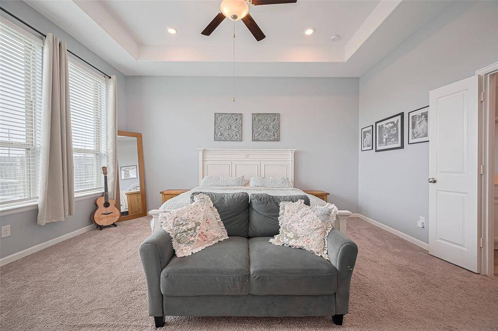The spacious primary suite features a tray ceiling, large windows, and soft carpet for a relaxing retreat. The amount of natural light and stylish finishes add to the room’s serene and inviting ambiance.