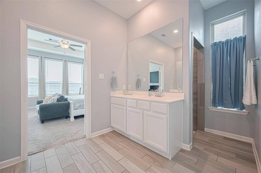 The primary's en suite bath showcases dual vanities with expansive counterspace and modern fixtures. A large window brightens the space while a private walk-in shower adds functionality and style.