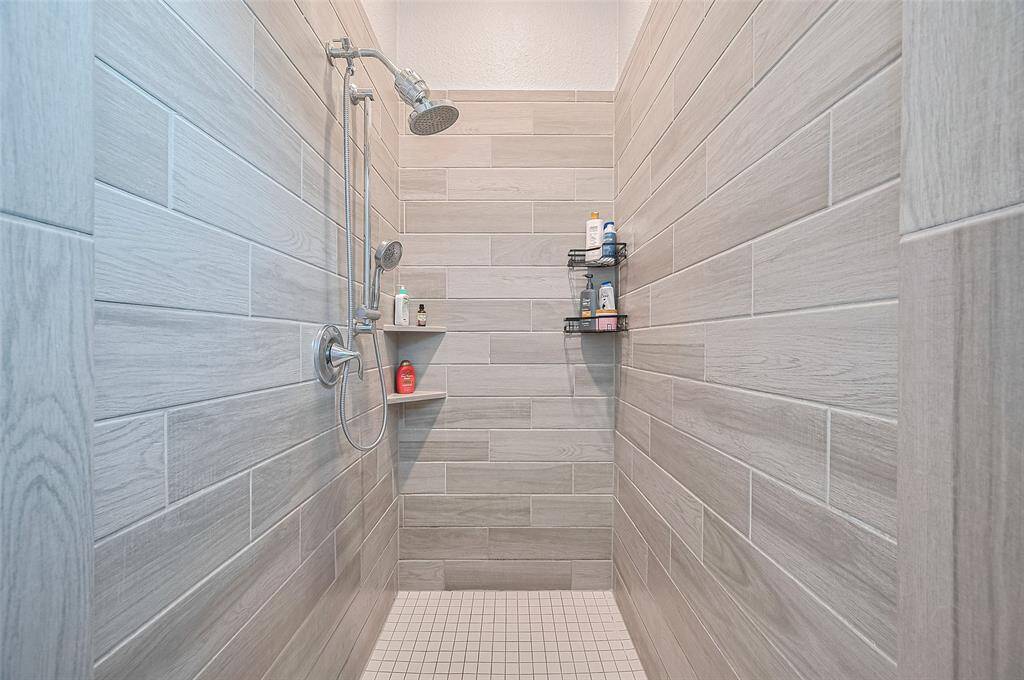 This spacious walk-in shower showcases sleek tilework and built-in shelving for added convenience. A rainfall-style showerhead completes the spa-like experience.