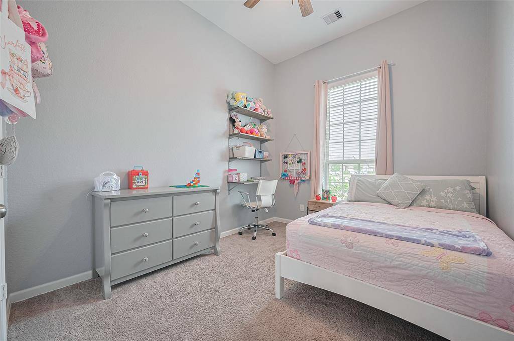 This charming bedroom features soft gray walls, a plush carpet, and natural light from a large window. Built-in shelving and ample space make it ideal for both rest and creativity.