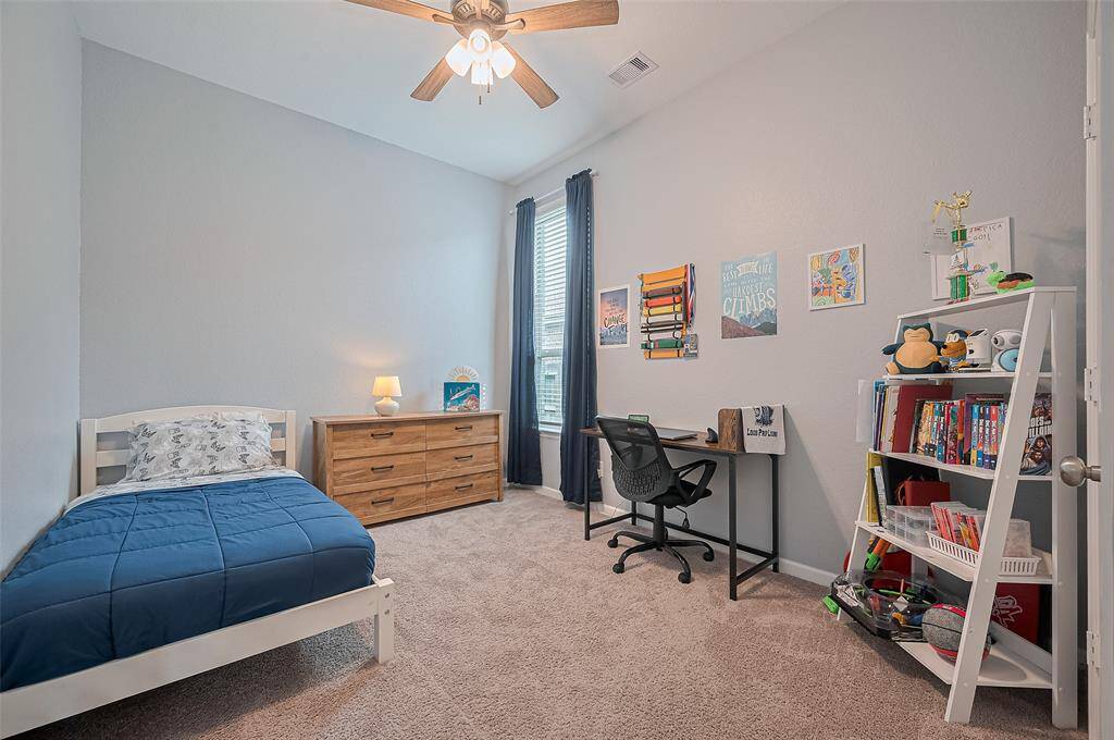This spacious secondary bedroom features a high ceiling and cozy carpet flooring. A large window brings in plenty of natural light, while the layout offers both a restful sleeping space and a functional study area.