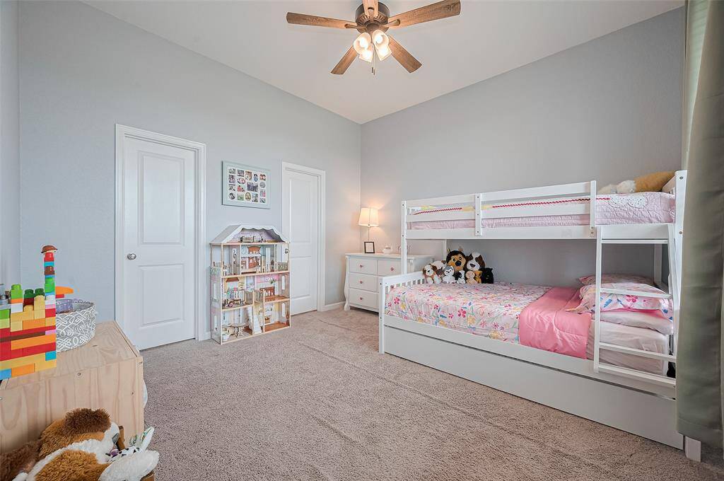 A third secondary bedroom shows more space for rest and play, complete with a bed space and carpet. Neutral walls and a ceiling fan provide comfort, while the setup invites creativity and fun.