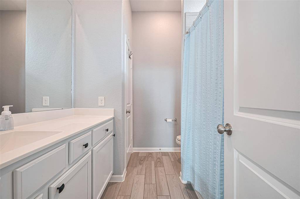 The en suite bathroom features a wide vanity with ample storage and a nice, integrated sink. A soft blue shower curtain adds a calming touch to the clean, modern design.