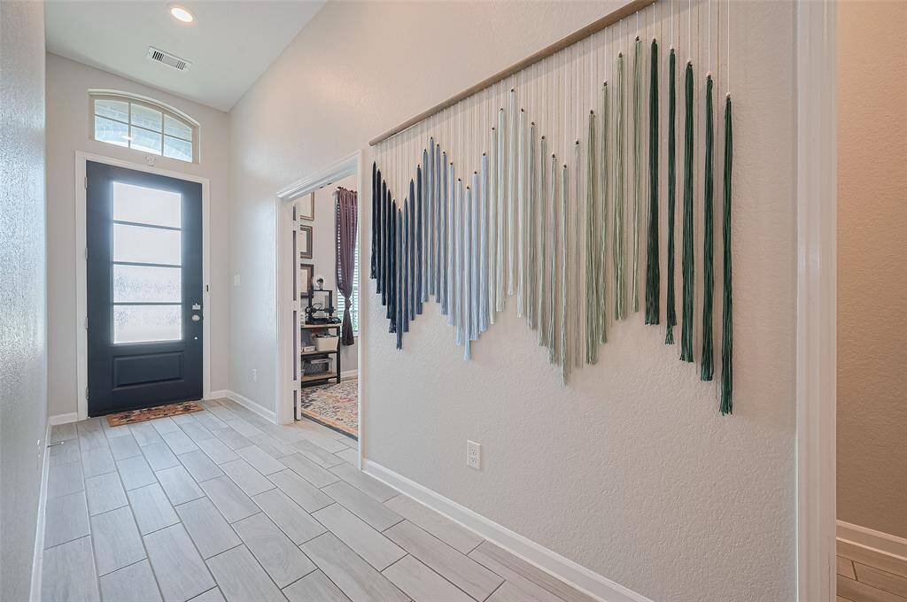 bright and inviting foyer features sleek tile flooring and a modern glass-paneled front door that fills the space with natural light. The tall ceilings and soft neutral tones create an open, airy atmosphere perfect for welcoming guests.