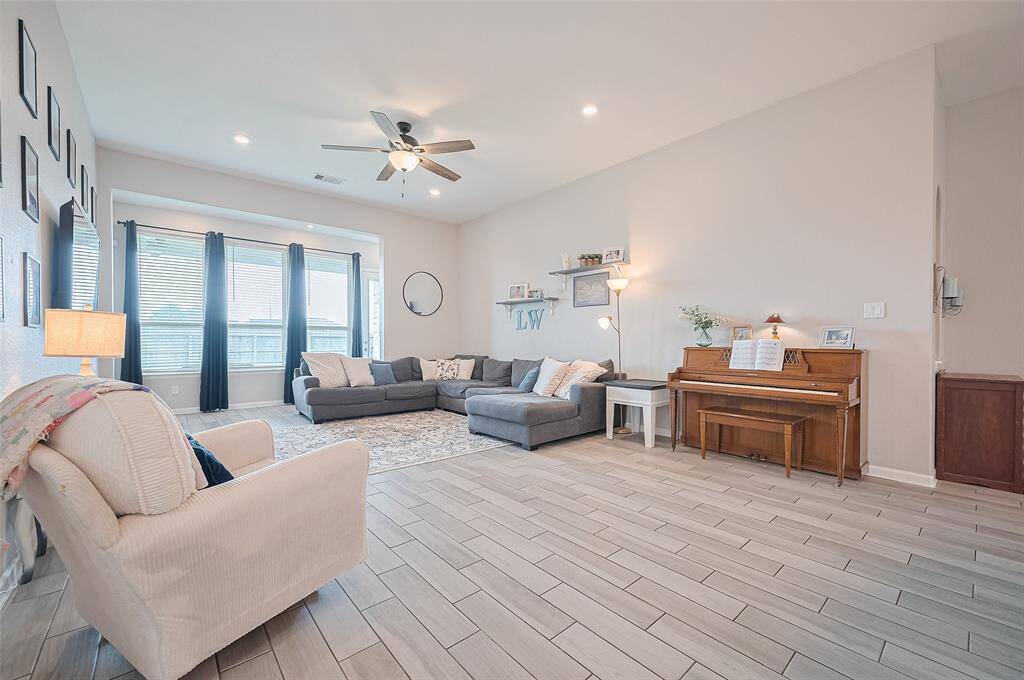 Expansive great room offers an abundance of natural light through a wall of large windows, creating a bright and airy atmosphere. High ceilings and recessed lighting enhance the sense of openness and modern comfort.