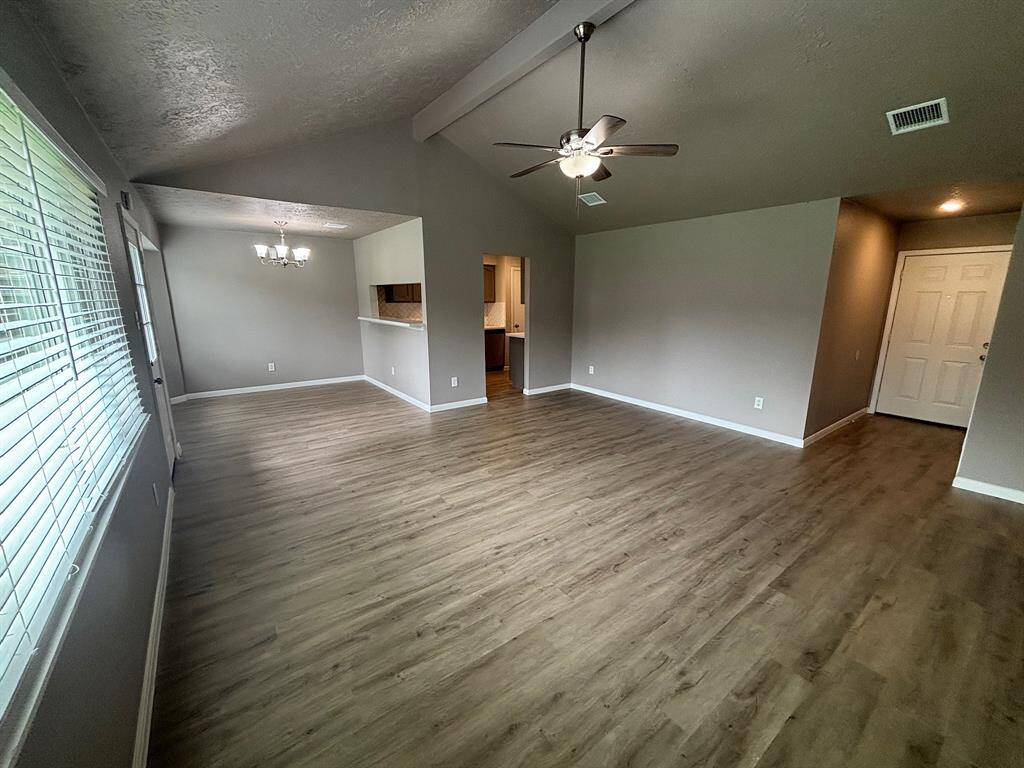 Bright and spacious open-plan living area with laminate wood flooring, neutral walls, and a ceiling fan. Features a dining space with a modern light fixture and a pass-through to the kitchen. Large windows provide ample natural light.