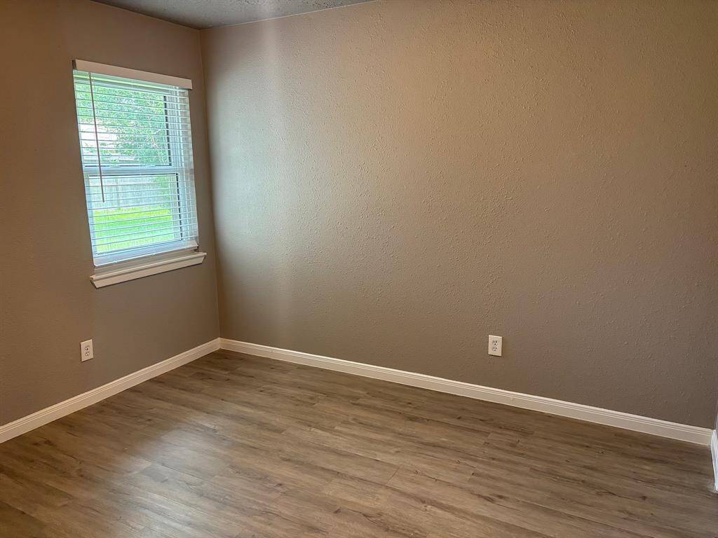 This bedroom features neutral walls, a window with blinds for natural light, and wood-look flooring, creating a cozy and versatile space.