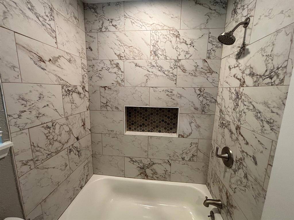 Primary bathroom featuring elegant marble-style tiles, a sleek shower head, and a convenient built-in niche for essentials.