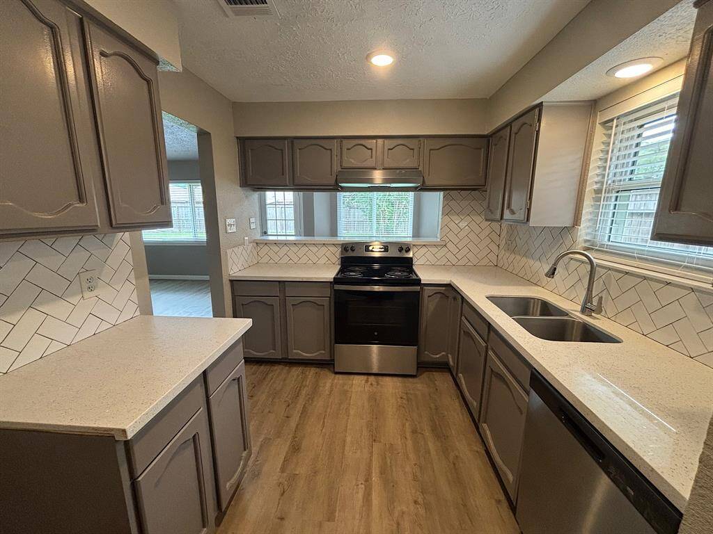 It includes stainless steel appliances, recessed lighting, and a large window for natural light. The wood-look flooring adds warmth and elegance.