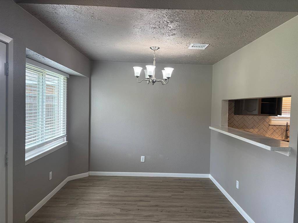 Discover a modern dining space featuring elegant wood-look flooring, neutral gray walls, and a chic chandelier. Enjoy abundant natural light through the window and the convenience of a kitchen bar.
