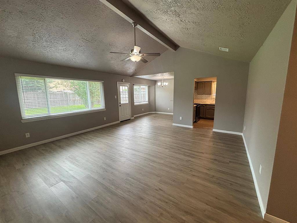 This inviting living space boasts vaulted ceilings, abundant natural light from large windows, and light wood flooring. The open layout seamlessly connects to the dining area and kitchen, enhanced by modern neutral tones.