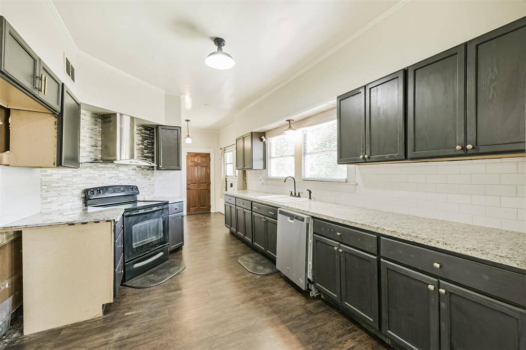 Spacious kitchen with dark cabinetry, granite countertops, and stainless steel appliances. Features a modern backsplash, large windows for natural light, and wood-look flooring.