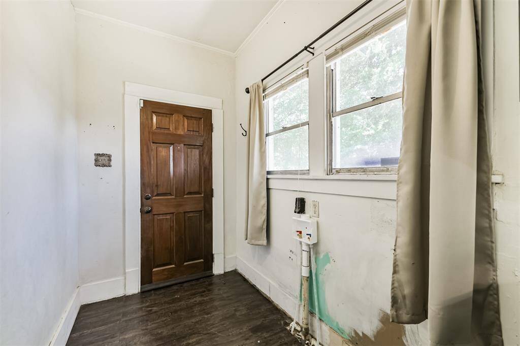 This photo shows a small laundry area with laminate wood flooring and two windows with curtains.