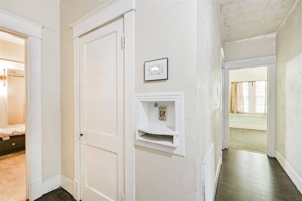 This photo shows a hallway with white walls and doors, featuring a built-in phone/phonebook nook and a glimpse into adjacent rooms with natural light. The floors are dark, offering a clean and simple aesthetic.