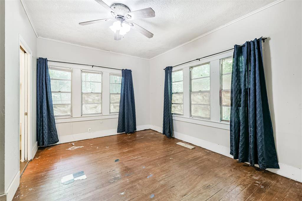Bright room with multiple windows, hardwood floors, and ceiling fan. Blue curtains add a touch of color. Some floor and wall repairs needed, offering a customizable space. This room also has an en-suite 1/2 bathroom.