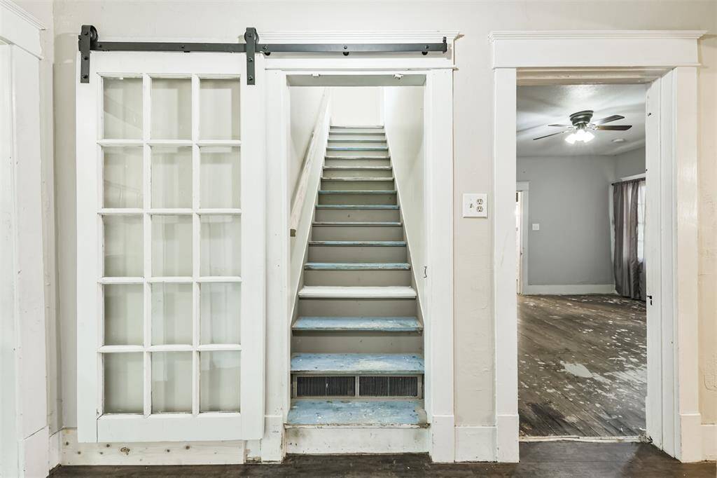 This photo features an interior view with a sliding barn door on the left, revealing a narrow staircase with painted steps.
