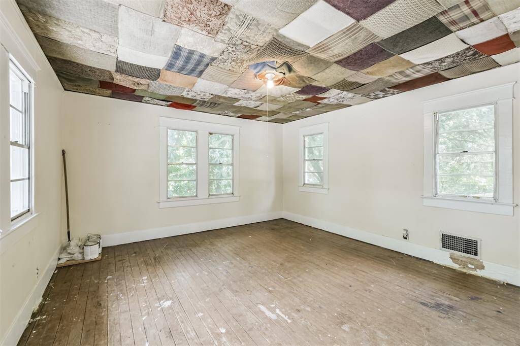 This room features a unique patchwork ceiling, three windows providing natural light, and wooden floors. It has a rustic, unfinished look with potential for customization.