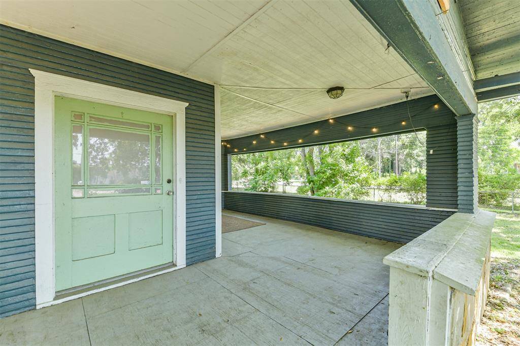 Charming covered porch with a retro green door, string lights, and a spacious sitting area. Surrounded by lush greenery, perfect for relaxing or entertaining.