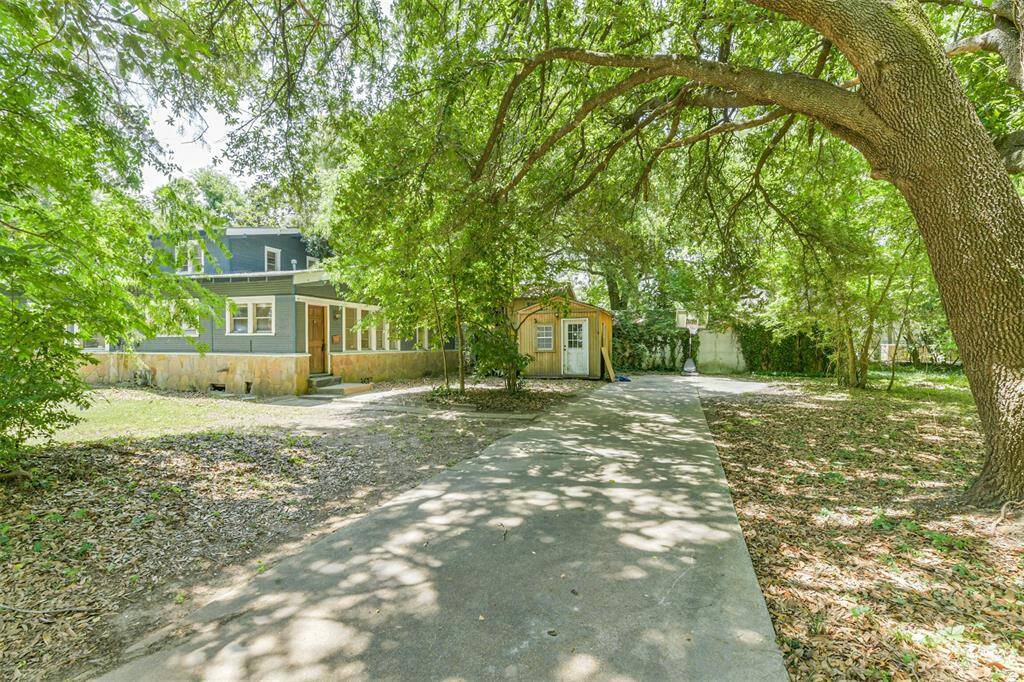 This photo showcases a charming home with a spacious, shaded driveway surrounded by lush trees. The house features a cozy porch and a detached shed, offering plenty of potential for outdoor activities and storage.