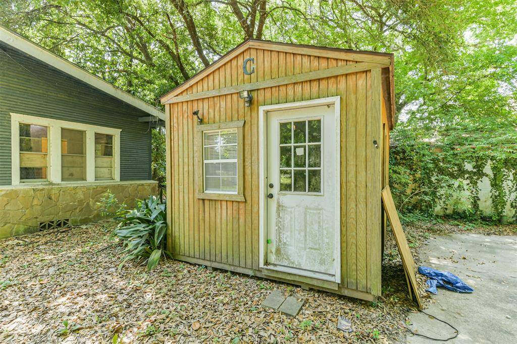 This photo features a small wooden shed with a single window and a white door, situated beside the house. The area is surrounded by trees and foliage, creating a natural, secluded atmosphere. Perfect for extra storage or a potential workshop space.