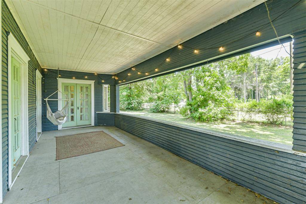 This inviting porch features a cozy hammock chair and a spacious layout with a view of lush greenery, perfect for relaxing or entertaining.