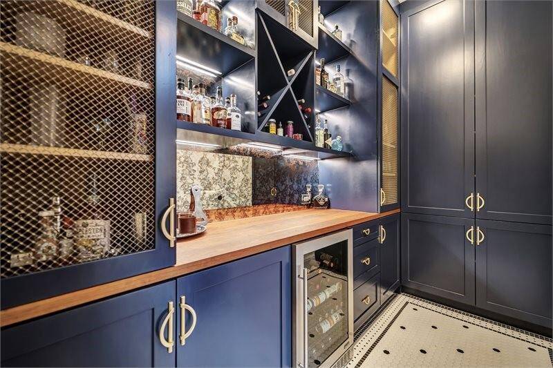 Stylish bar features custom cabinetry, a built-in wine fridge, shelving with accent lighting, and a beautiful wood countertop—perfect for entertaining and storage.