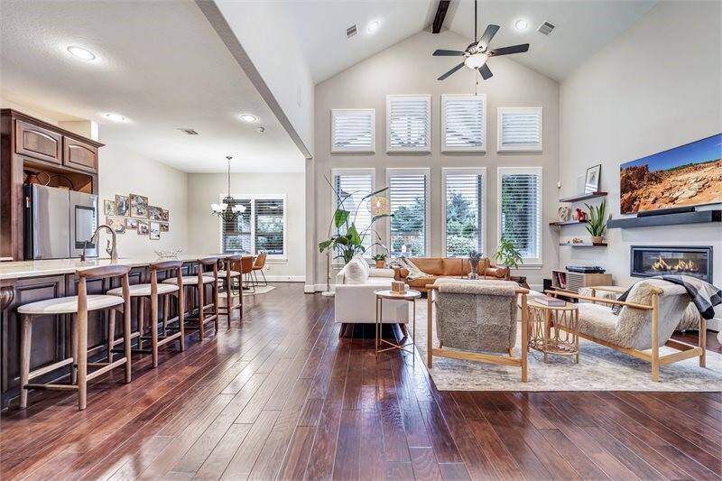 Spacious open-concept living area features prominent ceilings and a wall of windows for abundant natural light with access to the kitchen with a large island and bar seating—perfect for entertaining and everyday living.