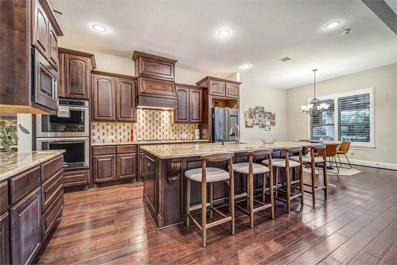 Gourmet kitchen features rich wood cabinetry, granite countertops, a large island with bar seating, and an open layout that flows into a bright breakfast area.
