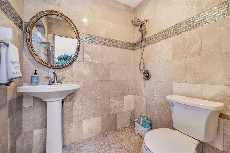Full outdoor wet bathroom with hot-water shower, sink, toilet, and floor to ceiling Italian marble tile.