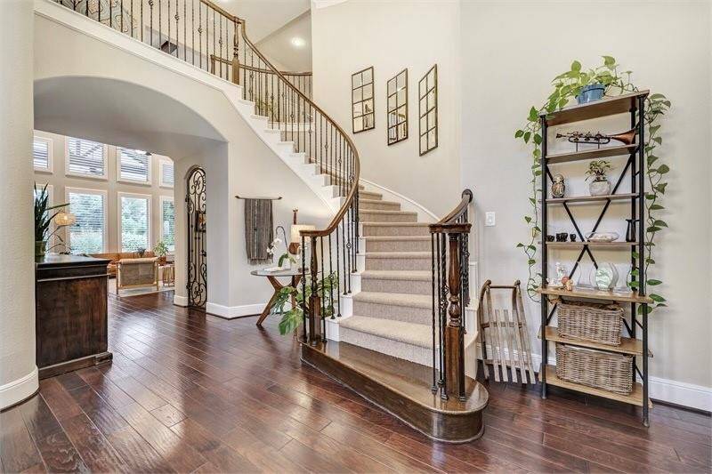 Elegant entryway features a grand curved staircase, rich engineered hardwood floors, and abundant natural light, creating a warm and inviting first impression.