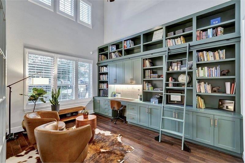 Stunning downstairs study features soaring ceilings, custom built-ins in 2022 with  including a rolling ladder to easily reach all the bookshelves. Abundant natural light, and a cozy seating area—perfect for work or relaxation.