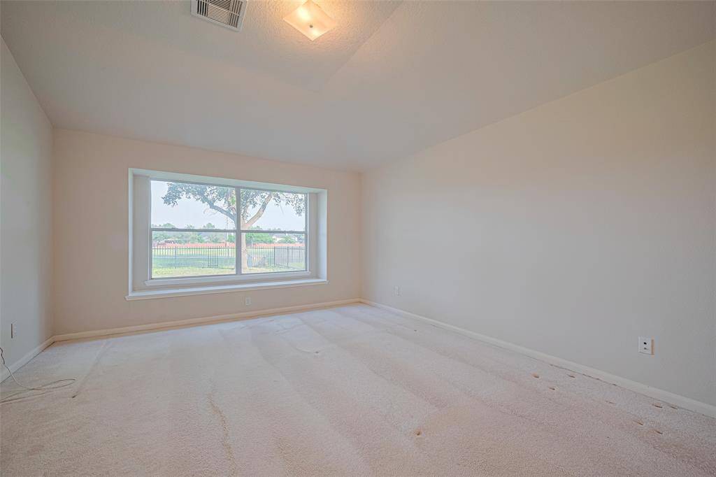 Expansive yet serene, the primary suite offers a wide window with views of green, a recessed ceiling for architectural interest, and plush carpeting that underscores its comfort.