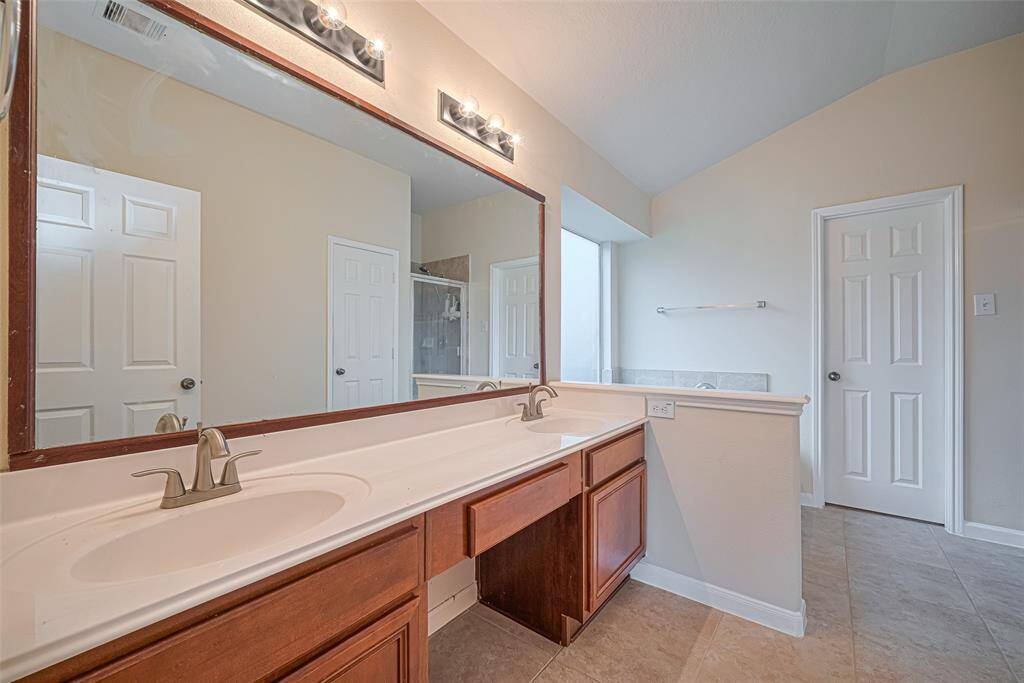 A spacious en suite features dual sinks under a large mirror, a soaking tub set beneath a frosted window, and a separate glass-enclosed shower—both spa-like and practical.