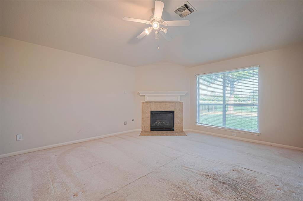 Anchored by a classic fireplace and a large window that floods the space with light, this living area offers comfort in abundance, with a ceiling fan for added breeze and balance.