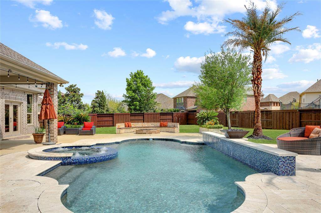 A backyard retreat awaits with a sparkling pool, elevated spa, and spacious patio framed by lush greenery. A covered porch offers a shady spot to unwind or entertain, while mature trees and a privacy fence complete the tranquil setting.
