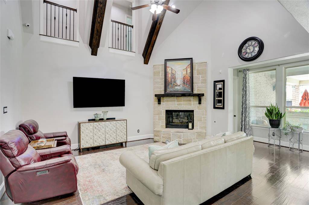This soaring living room impresses with vaulted ceilings, exposed wood beams, and a stone fireplace. Soft seating and natural light complete this welcoming, spacious retreat.