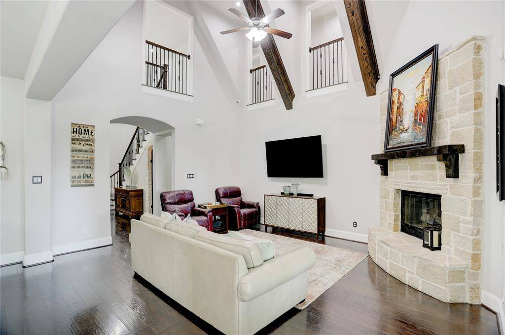 A blend of rustic charm and comfort, this living room features vaulted ceilings, exposed beams, a stone fireplace, and open flow to the staircase. Dark wood floors add richness to the space.