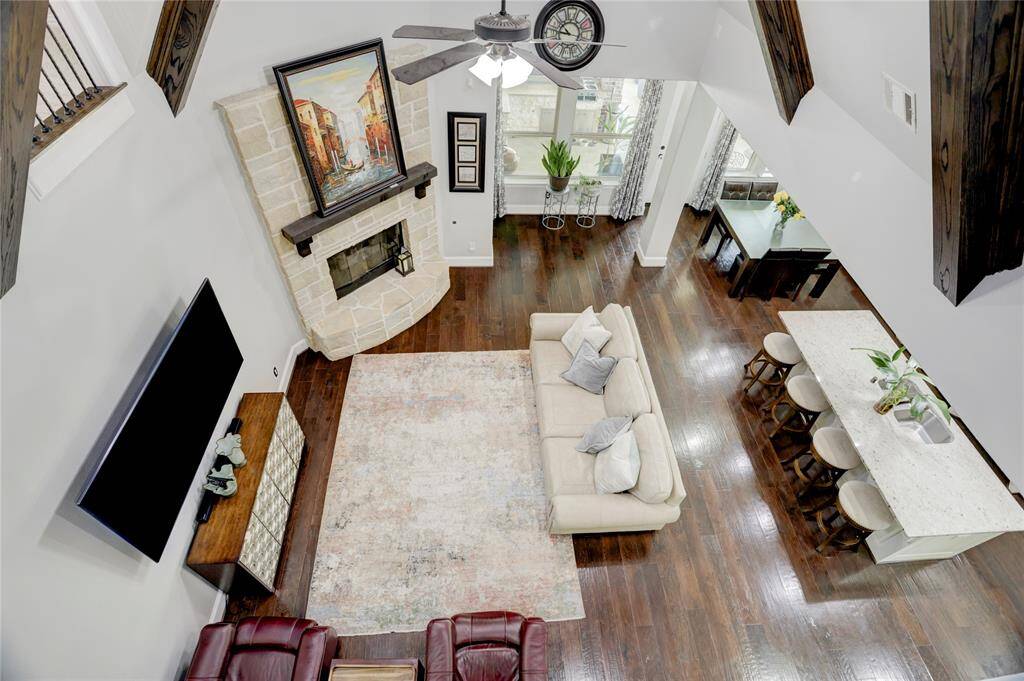 This open living area offers high ceilings, dark hardwood floors, and a comfortable sectional by the fireplace. The kitchen with bar seating and stainless appliances enhances the seamless flow of the space.