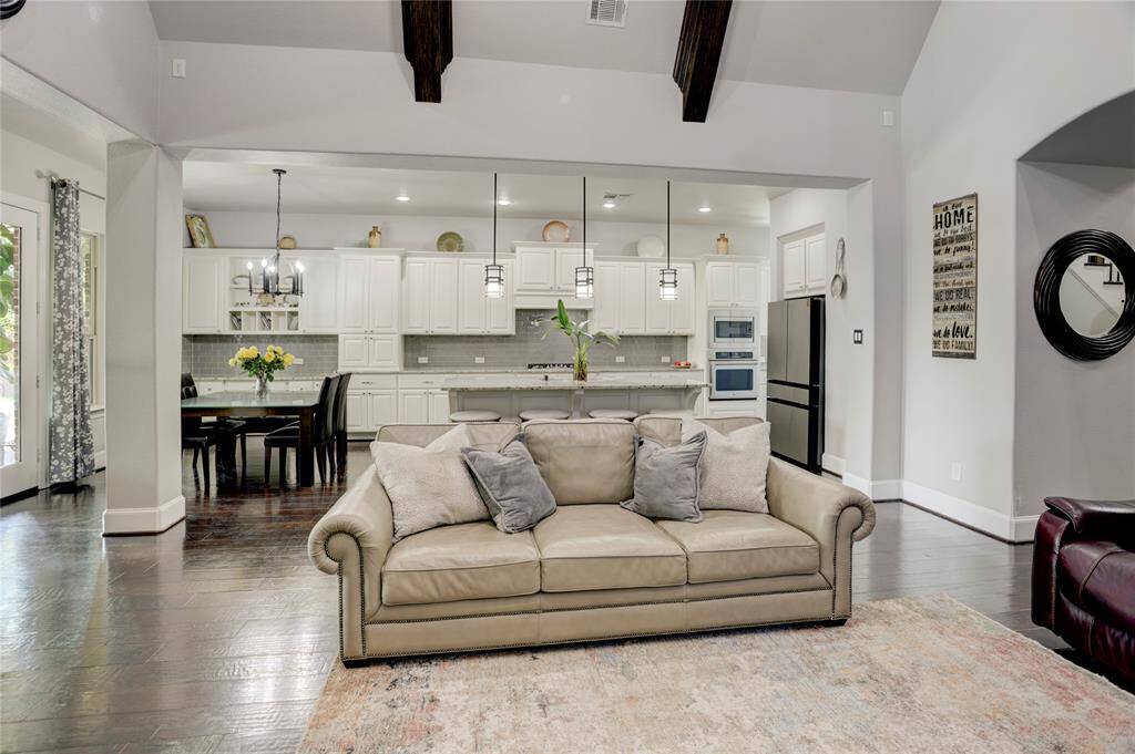 A bright, inviting layout pairs a cozy sofa and dark wood floors with a crisp white kitchen. The nearby dining area enjoys sunlight from expansive windows.