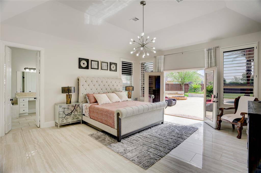 The airy primary bedroom offers tile floors, a tufted headboard, and large windows with patio access. A modern chandelier and spa-inspired bath complete the relaxing retreat.
